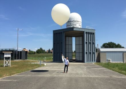 In the picture, a man is holding a string to which a floating weather balloon is attached.