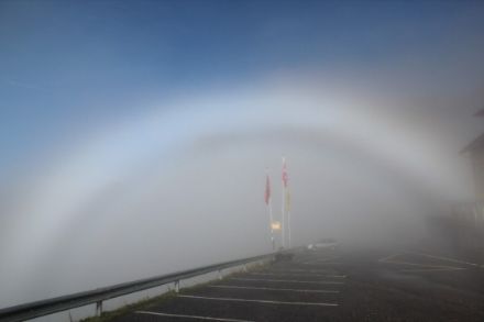 Image of an fog bow glowing white: above the fog bow, the cloudless sky can be seen.