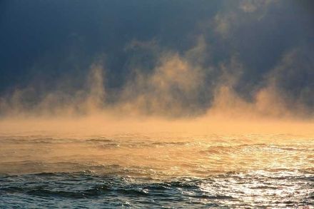 Evaporation fog over a lake, glowing orange in the sunlight.