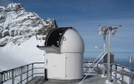 Photography of the SACRaM station showing an astronomical cupola protecting radiation instruments on top of the Sphinx building at Jungfraujoch. A 3-meter tall measurement bench is on the right of the picture supporting radiometers measuring UV, global solar and thermal infrared irradiance.